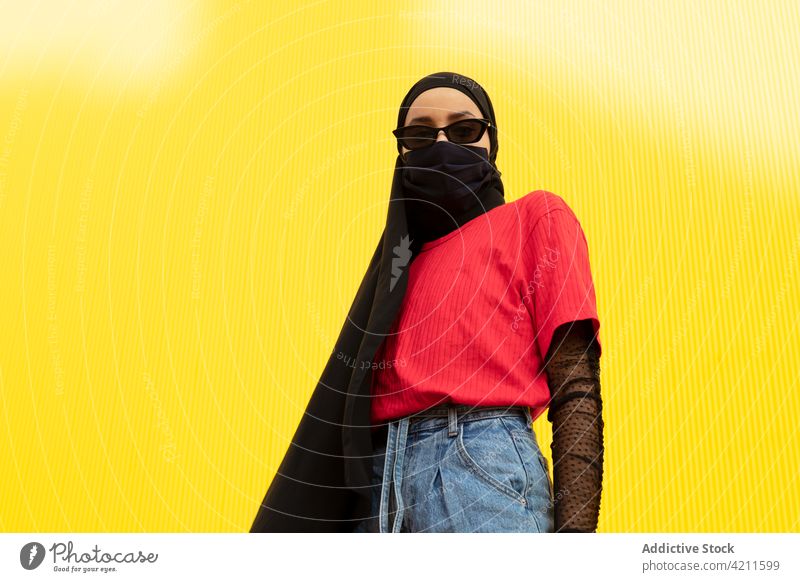 Trendige muslimische Frau mit Sonnenbrille auf gelbem Hintergrund Mode Stil Individualität Kopftuch cool Mundschutz Porträt farbenfroh Bund 19 Stoff