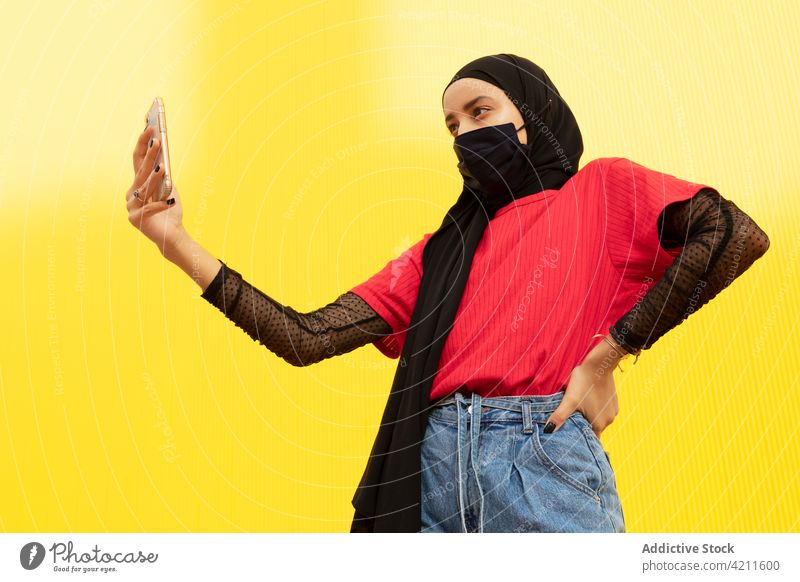 Trendige muslimische Frau mit Gesichtsmaske, die ein Selfie mit ihrem Smartphone macht Selbstportrait trendy Mode cool Individualität Hand an der Hüfte Porträt
