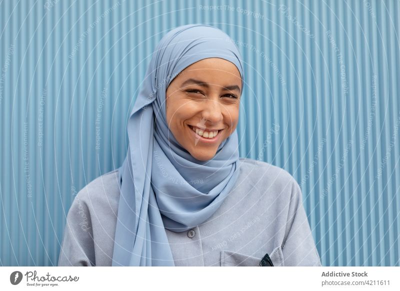 Glückliche ethnische Frau mit Kopftuch auf blauem Hintergrund Melancholie wehmütig einsam herzlich nachdenken Islam Porträt Stil lässig modern Farbe