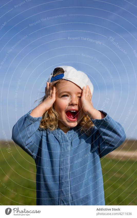 Aufgeregtes Mädchen mit Mütze in der Natur Sommer Wiese aufgeregt Tastkopf Blauer Himmel Mund geöffnet Verschlussdeckel Stil blond Kind Glück heiter Vergnügen