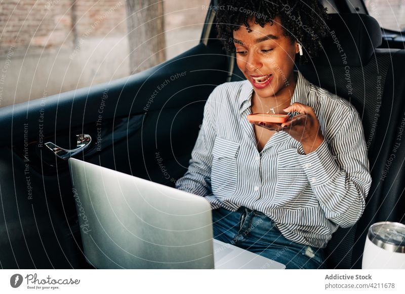 Junge schwarze Frau benutzt Smartphone und Laptop im Auto benutzend PKW Glück Lächeln Audio Mitfahrgelegenheit Netbook Taxi Arbeit Arbeitsweg jung Job abgelegen