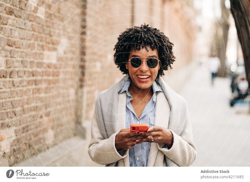 Lächelnde schwarze Frau mit Smartphone benutzend Glück Anschluss Spaß Freude digital sorgenfrei Internet Browsen Mobile Telefon froh Inhalt Apparatur positiv