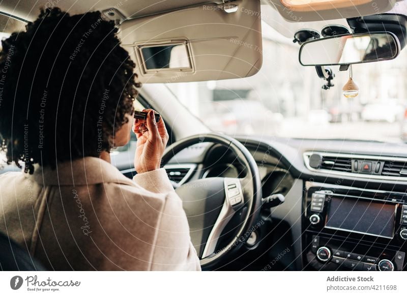 Schwarze Frau trägt im Auto Lippenstift auf Fahrer bewerben Spiegel Make-up PKW Routine Schönheit verwöhnen Automobil Verkehr Vorschein Kosmetik feminin Gesicht