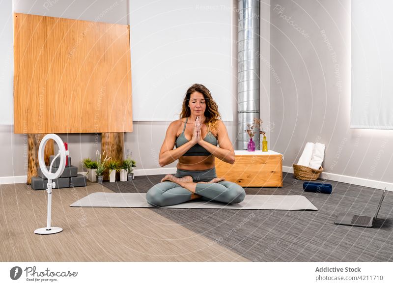 Meditierende Frau in der Yogastellung Padmasana padmasana Lotus-Pose meditieren vlog Augen geschlossen Smartphone Stativ Gebetshände Blogger üben jung