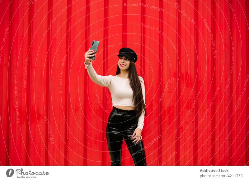 Lächelnde stilvolle Geschäftsfrau nimmt Selfie in der Stadt Großstadt heiter Unternehmer Stil trendy Gedächtnis Selbstportrait Smartphone Frau rot Wand Straße
