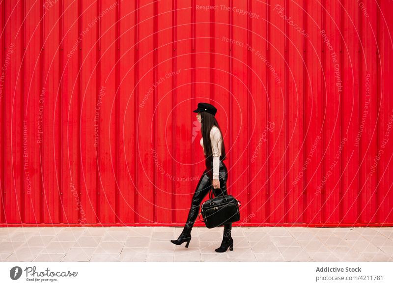 Stilvolle Geschäftsfrau zu Fuß entlang der Straße in der Stadt Unternehmer Spaziergang Großstadt gut gekleidet trendy Bürgersteig urban Frau Outfit rot Wand