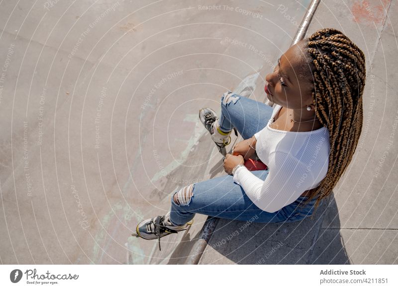 Stilvolle ethnische Frau in Rollschuhen im Skatepark Rollerblade Skateplatz cool Sommer Hobby trendy Rampe Geflecht schwarz Afroamerikaner Jeansstoff sorgenfrei