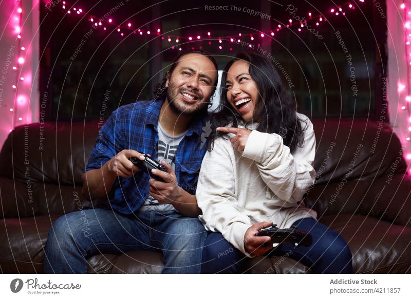 Entzücktes ethnisches Paar spielt zusammen ein Videospiel Freude spielen aufgeregt Liege Steuerkreuz Spaß haben unterhalten Zusammensein Lachen Gamepad Spiel