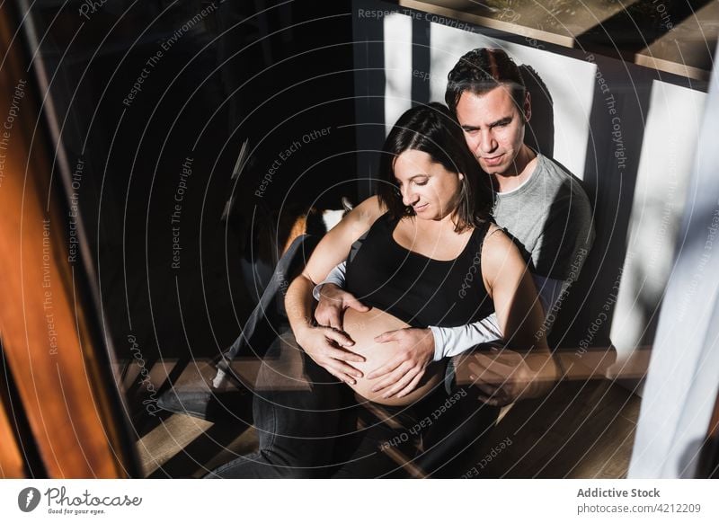 Friedliches Paar sitzt und kuschelt zu Hause auf dem Boden Umarmung schwanger Zusammensein Angebot erwarten Schwangerschaft Bauch berühren Gelassenheit