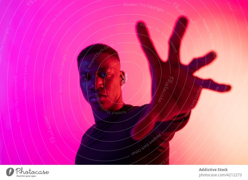 Selbstbewusster afroamerikanischer Mann streckt im Studio die Hand zur Kamera aus selbstbewusst neonfarbig ausdehnen sich[Akk] melden stoppen Studioaufnahme