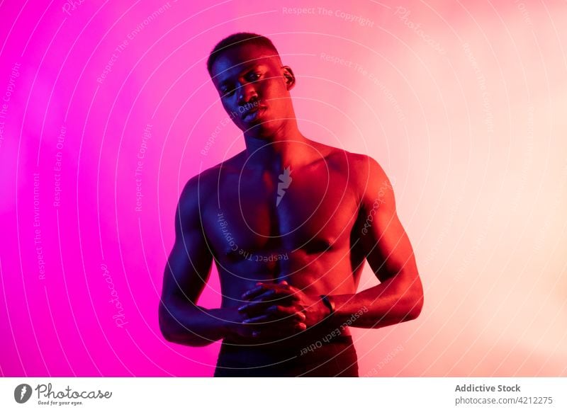 Emotionsloser schwarzer Mann ohne Hemd auf rosa Hintergrund sportlich muskulös ernst Athlet emotionslos neonfarbig Studioaufnahme selbstbewusst Afroamerikaner