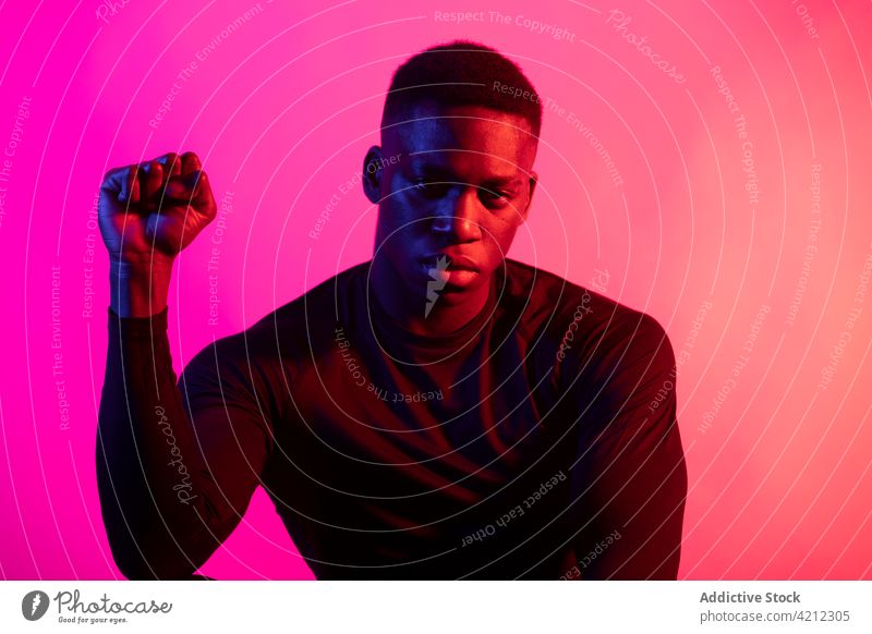 Seriöser afroamerikanischer Mann im Neonstudio ernst neonfarbig emotionslos Studioaufnahme Faust sportlich Athlet Persönlichkeit allein Porträt selbstbewusst