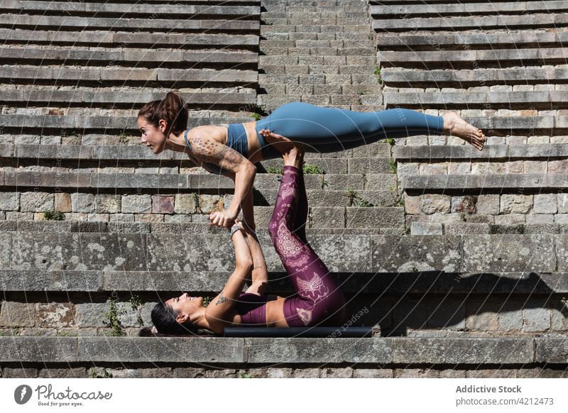 Fitte Frauen machen gemeinsam Akro-Yoga auf der Matte üben akrobatisch abstützen Gleichgewicht beweglich Asana Zusammensein Wohlbefinden Vitalität Harmonie