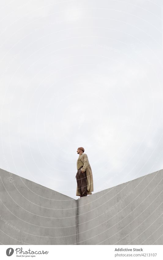 Mann steht am Rande einer Betonmauer einsam grau Himmel Wand Einsamkeit Stimmung Melancholie Atmosphäre männlich Hand-in-Tasche allein nachdenken Windstille