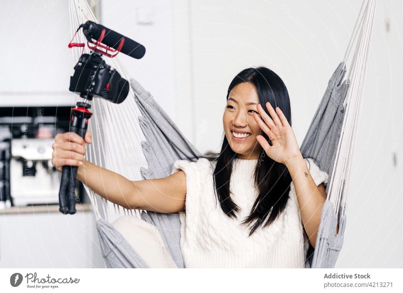 Fröhliche asiatische Bloggerin, die auf einer Hängematte ein Video mit einer Fotokamera aufnimmt Vlogger Aufzeichnen Fotoapparat heiter soziale Netzwerke Frau