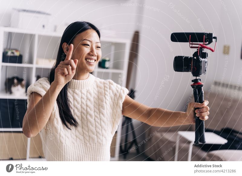 Fröhliche asiatische Bloggerin, die auf dem Sofa ein Video mit einer Fotokamera aufnimmt Vlogger Aufzeichnen Fotoapparat heiter soziale Netzwerke Frau benutzend