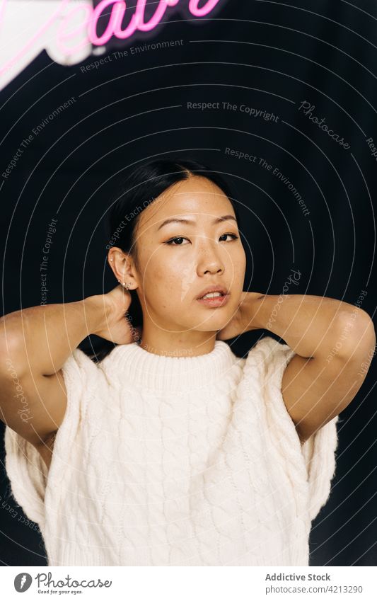 Asiatische Frau steht unter Inschrift auf schwarzem Hintergrund Stil lässig Individualität feminin Aufschrift Porträt asiatisch ethnisch Ornament Bekleidung