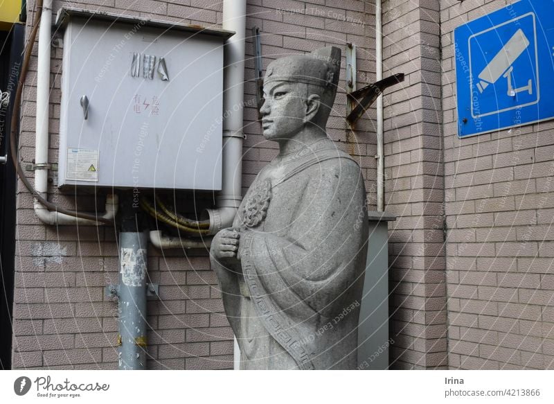 Eine chinesische Statue und Videoüberwachung in Shanghai. China Steinstatue Überwachungsstaat Kontrolle bewachen Chinesisch Mönch Hinweisschild Hausmauer Gasse