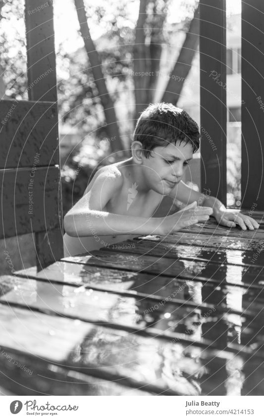 Junge klettert in Holzspielzeug, um in einer Wasserpfütze zu spielen; sensorisches Spiel für Kind mit Autismus Wasserspiel Pfütze Spielset Aufstieg Spielplatz