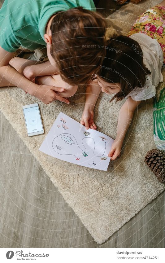 Draufsicht auf Kinder, die zu Hause auf dem Teppich Schatzsuche spielen unkenntlich Schatzsuchspiel mobiler Kompass heimwärts Landkarte Blick Familie Freizeit