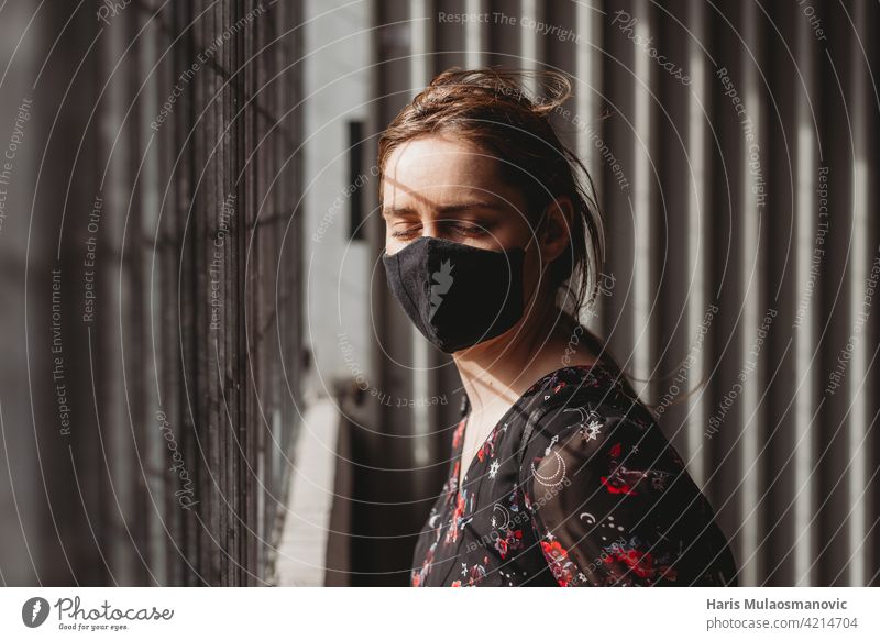 depressive Frau mit Gesichtsmaske hinter Metallstäben geschlossene Augen auf die Sonne Strahlen Erwachsener Amerikaner Angst apokalyptisch schwarz atmen