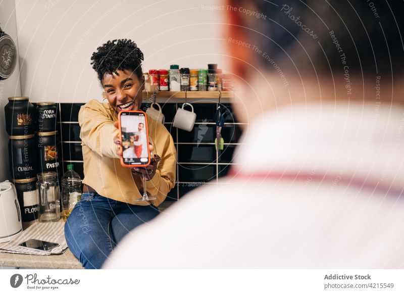 Lächelnde schwarze Frau zeigt Foto auf Smartphone für Freund Paar Spaß haben zeigen teilen heiter Zusammensein Küche multiethnisch rassenübergreifend vielfältig