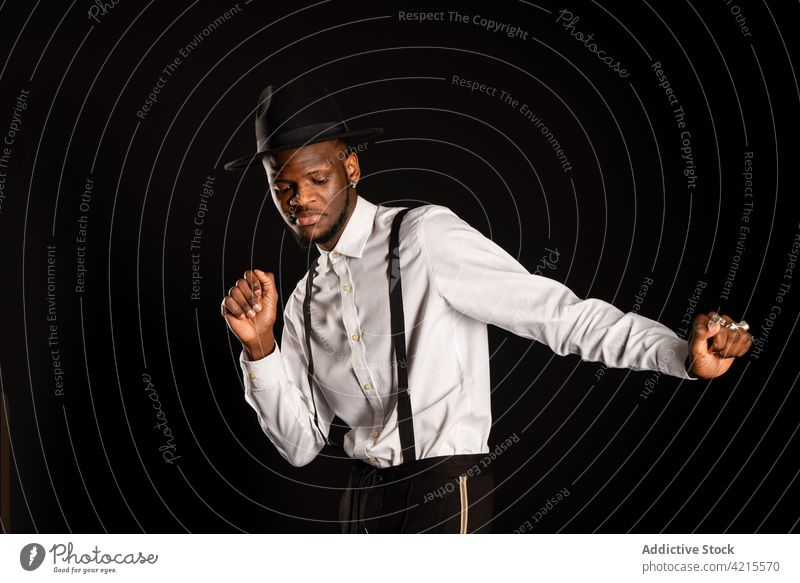 Stilvoller schwarzer Mann in weißem Hemd und Hut tanzt auf schwarzem Hintergrund Model gut gekleidet Kavalier Glück Tanzen maskulin Porträt Macho Kleidungsstück