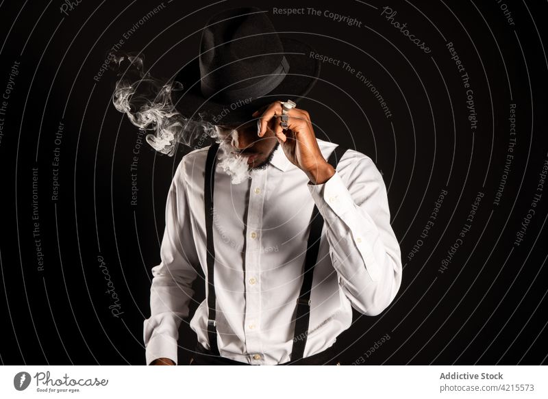 Stylish ethnischen Mann vaping auf schwarzem Hintergrund Raps e Zigarette Rauch Nikotin ausatmen Stil maskulin diffus Porträt Mode Individualität Macho viril