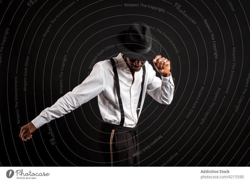 Stilvoller schwarzer Mann in weißem Hemd und Hut tanzt auf schwarzem Hintergrund Model gut gekleidet Kavalier Glück Tanzen maskulin Porträt Macho Kleidungsstück