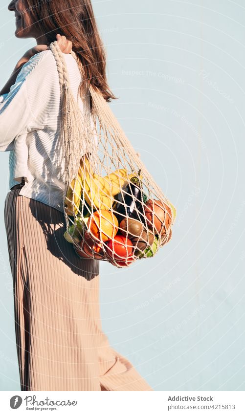 Fröhliche Frau mit Netzbeutel voller reifer Lebensmittel Lebensmittelgeschäft ineinander greifen Tasche Baumwolle umweltfreundlich keine Verschwendung Frucht