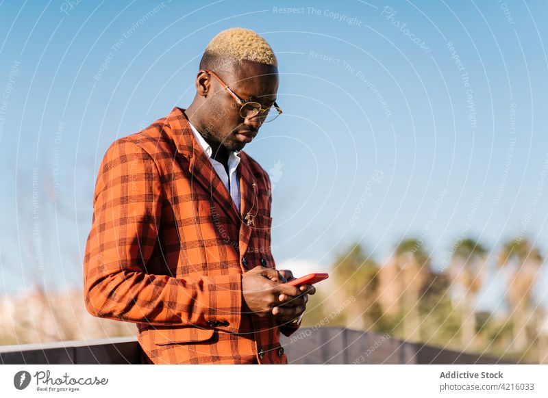 Trendiger schwarzer Mann, der in der Stadt eine SMS auf seinem Smartphone schreibt Mode Tartan Stil kariert blond benutzend Apparatur Afroamerikaner Gerät