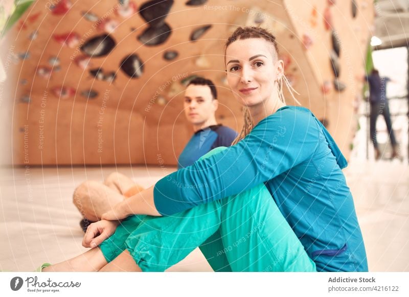 Lächelnde Kletterer in der modernen Boulderhalle Sportlerin Aufsteiger Zentrum Felsbrocken Athlet Aufstieg Wand künstlich heiter Fitnessstudio sitzen Stock