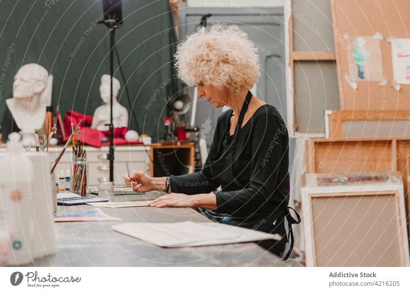 Ernste Frau malt auf Papier im Kunstatelier Künstler Farbe Anstreicher Wasserfarbe Pinselblume Werkstatt Handwerkerin kreativ Atelier Fokus ernst Talent