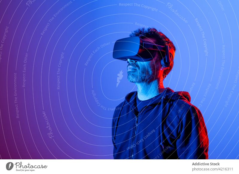 Anonymer Mann erlebt virtuelle Realität in einer Schutzbrille Headset VR erkunden eintauchen simulieren Technik & Technologie Entertainment neonfarbig benutzend