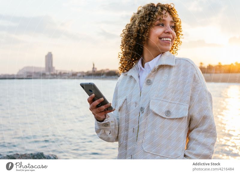 Schwarze Frau benutzt Mobiltelefon am Meer Meeresufer Sonnenuntergang Arme heiter Seeküste ethnisch schwarz Afroamerikaner Sommer Natur MEER Lächeln Ufer Abend