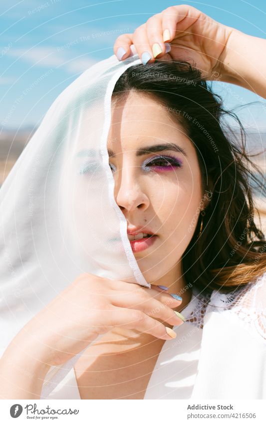 Braut mit Make-up unter blauem bewölktem Himmel im Sonnenlicht Auge abdecken Imkerschleier Hochzeit feiern brünett feminin sanft romantisch festlich Porträt