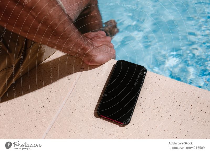 Crop-Mann mit Smartphone am Pool freiberuflich Beckenrand Sommer Urlaub abgelegen Telearbeit Entfernung männlich sitzen Anschluss Mobile Gerät Apparatur Telefon