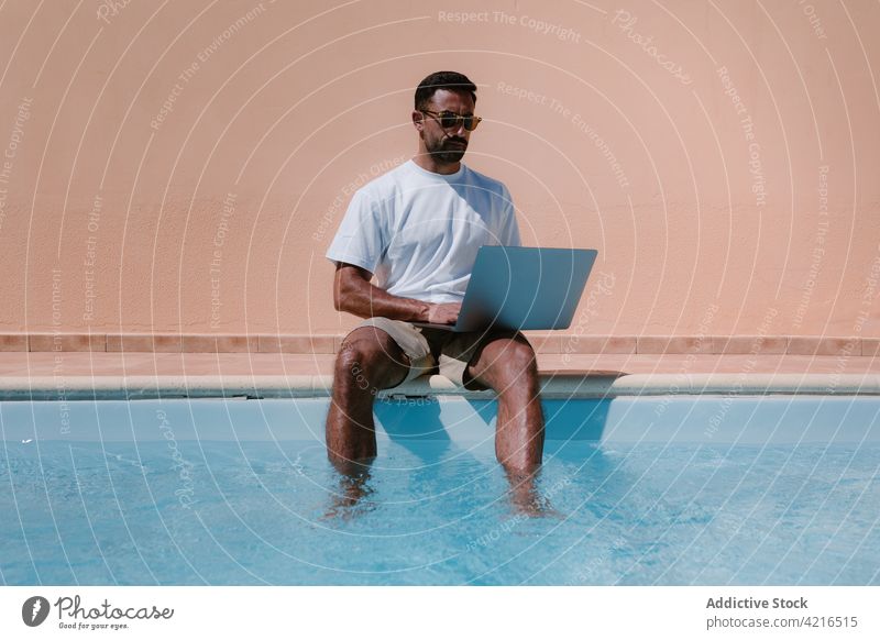 Mann benutzt Laptop am Pool freiberuflich Tippen Beckenrand Arbeit Telearbeit abgelegen Sommer männlich Urlaub benutzend Internet online Resort Surfen Browsen