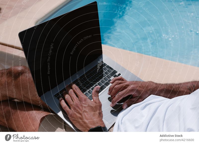 Anonymer Mann liegt auf einem Liegestuhl und surft auf einem Computer am Pool freiberuflich Beckenrand Telearbeit Browsen Sommer männlich Internet online