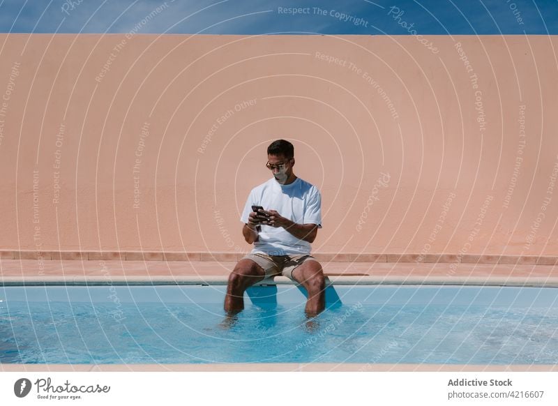 Männlicher Freiberufler, der am Pool mit seinem Smartphone spricht Beckenrand freiberuflich Mann sprechen Telearbeit Sommer Entfernung reden männlich Gerät