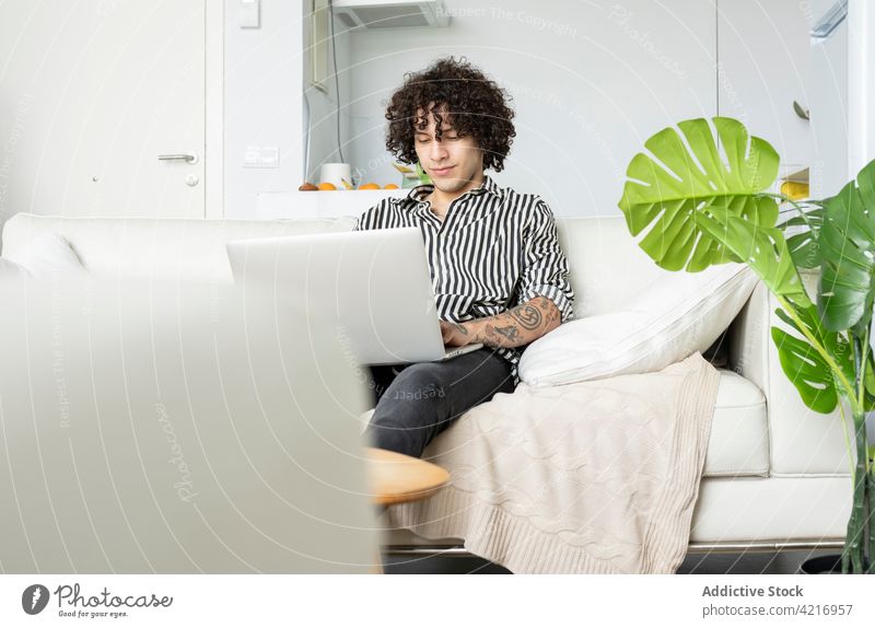 Tätowierter Mann surft im Internet auf einem Laptop auf dem Sofa zu Hause online Freizeit Surfen Tattoo heimwärts benutzend Apparatur Gerät zuschauend Kaffee