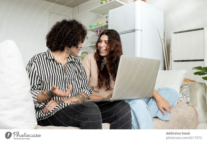 Zufriedenes Paar mit Laptop, das auf dem Sofa in der Wohnung spricht sprechen Zeit verbringen Wochenende Partnerschaft Tattoo herzlich heimwärts Apparatur Gerät