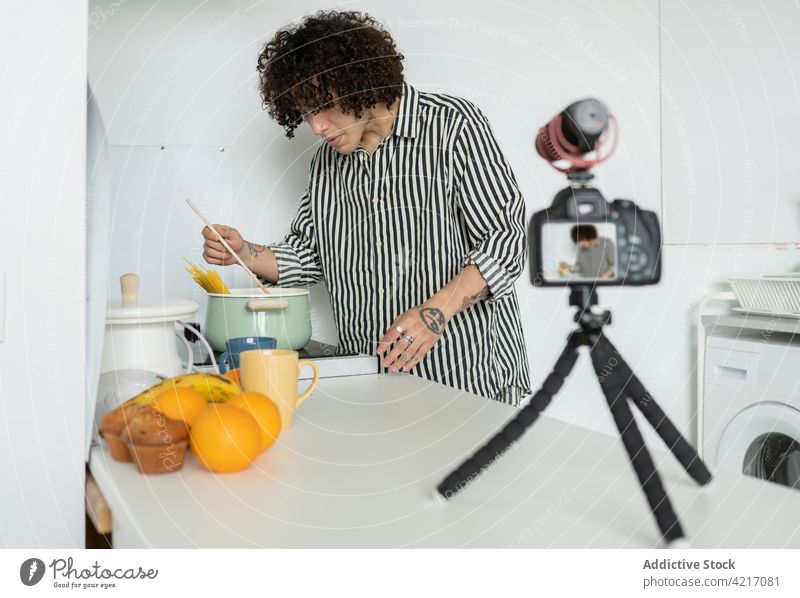 Vlogger mit Tattoos, der beim Kochen ein Video mit einer Fotokamera aufnimmt Aufzeichnen Fotoapparat kulinarisch sprechen Mann Küche benutzend Gerät Haus