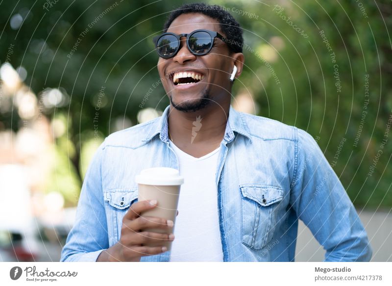 Mann hält eine Tasse Kaffee. Afrikanisch Amerikaner Straße Sonnenbrille Großstadt urban Konzept laufen Ohrhörer Ohrstöpsel Lächeln wegnehmen Freizeit Getränk