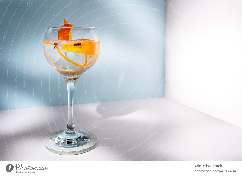 Glas Gin Tonic mit Orangenzesten auf dem Tisch Cocktail Alkohol hochball orange Schale Gewürznelke Schatten Wittern hell kreativ Design Wasser Aroma