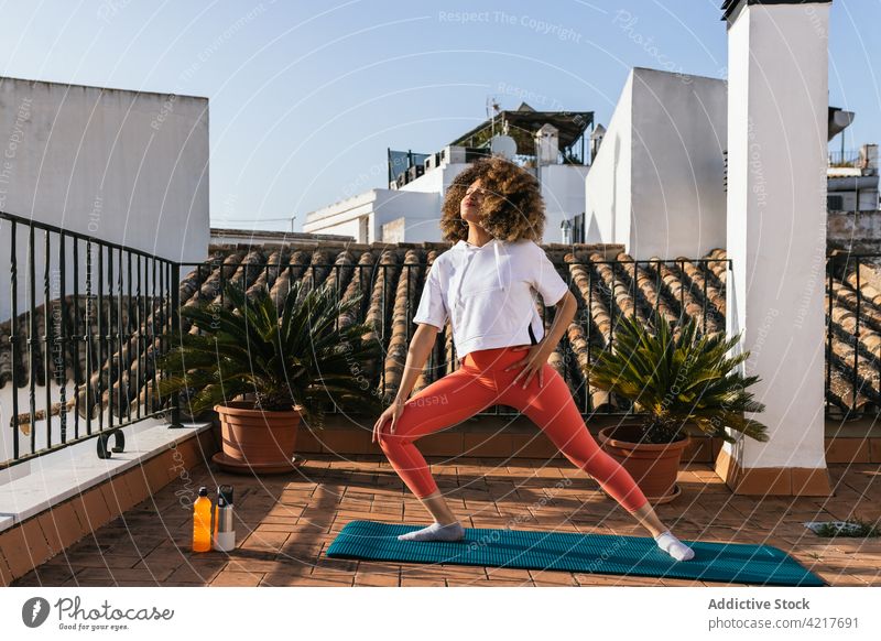 Schwarze Frau macht Yoga in Kriegerpose auf dem Dach Krieger-Pose Dachterrasse üben Training Asana Gleichgewicht sich[Akk] entspannen ethnisch schwarz