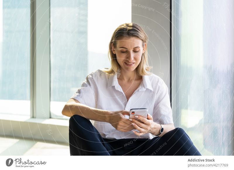 Frau in leerem Büro, die ein Smartphone benutzt schwarze Hose blond Glück Lächeln Gebäude nachdenklich Kaukasier Handy Textfreiraum Freude Gerät Mobile Telefon