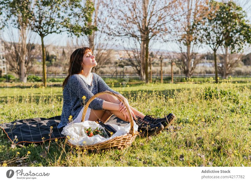 Verträumte Frau genießt Picknick an einem sonnigen Tag genießen Frühling Wiese Decke verträumt sorgenfrei Feld Knie umarmend Korb Glück Lächeln Gelassenheit