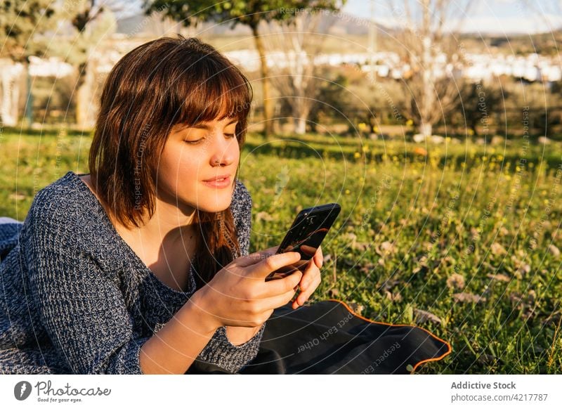 Frau auf Decke liegend beim Picknick im Park Frühling Smartphone benutzend Wiese sonnig genießen verträumt sorgenfrei sich[Akk] entspannen Natur ruhen Gerät