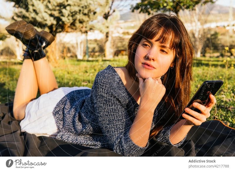 Frau auf Decke liegend beim Picknick im Park Frühling Smartphone benutzend Wiese sonnig genießen verträumt sorgenfrei sich[Akk] entspannen Natur ruhen Gerät